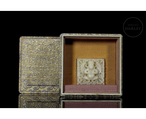 Carved jade, whitish with subtle reddish flecks. It is square, with relief decorations on the front face. It shows the deity 
