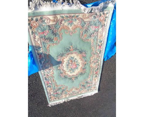 A handmade Chinese washed wool rug with central floral medallion and further decoration to border on pale jade green ground -