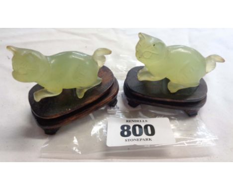 A pair of two small carved jade cats each set on hard wood stand