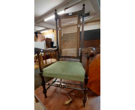 An old oak framed high back elbow chair with remains of rattan panel, open armrests and green upholstered seat panel, set on 