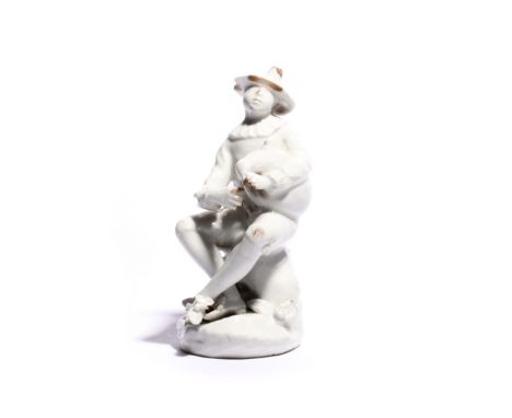 A Bow white-glazed figure of Harlequin c.1753-55, after the Meissen model by J J Kändler, seated on a rocky stump and playing