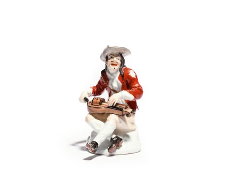 A Meissen figure of a beggar musician c.1740, modelled by Kändler, seated and playing the hurdy-gurdy, wearing a tattered red