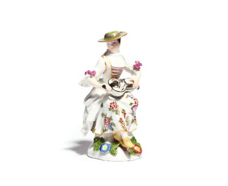 A Meissen figure of Columbine mid 18th century, seated and playing the hurdy-gurdy, the instrument resting in her lap, wearin