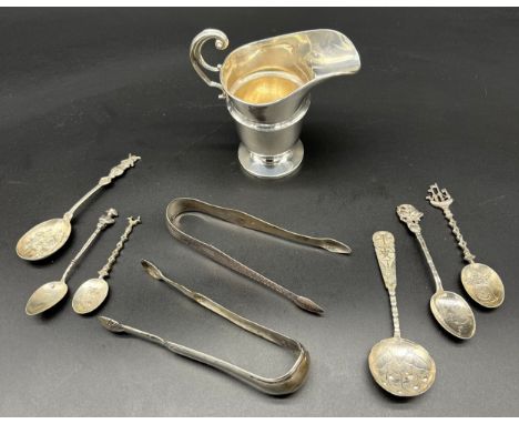 A Collection of silver items includes cream jug, Chinese caddy spoon, Georgian sugar tongs and various silver souvenir spoons