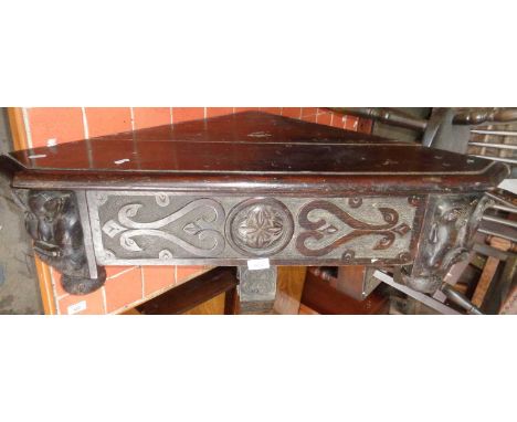 Victorian gothic carved oak corner shelf having bold carving of grotesque masks flanking a single drawer with chip carved sup