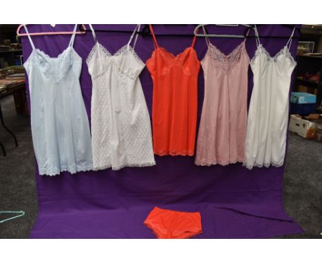 A collection of vintage nylon slips in a variety of colours, one having matching knickers.