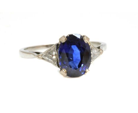 A platinum three stone sapphire and diamond ring, with an oval mixed cut sapphire, claw set at the centre, with a triangular 