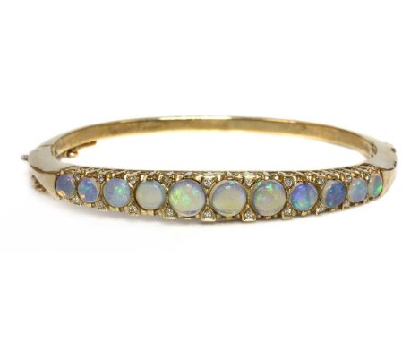 A 9ct gold opal and diamond hinged bangle,with a row of graduated circular cabochon opals, with pairs of brilliant cut diamon