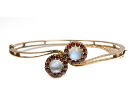 A gold moonstone and garnet cluster crossover bangle,with two circular cabochon moonstone and mixed cut garnets, in cut down 