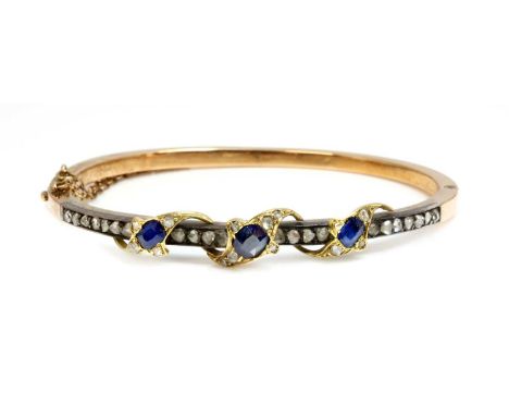 A sapphire and diamond hinged bangle,with a row of rose cut diamonds, grain set to the top half, three graduated yellow folia