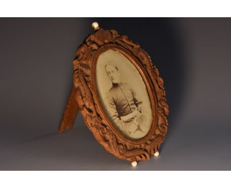 A Cantonese sandalwood oval easel photograph frame, carved with a ferocious dragon amongst scrolling clouds, enclosing a Worl