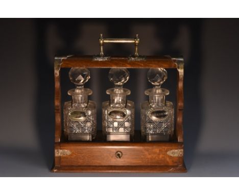 A Victorian Neo-Gothic EPNS-mounted oak three-bottle oak tantulus, cylinder carrying handle with ball finials, each rounded s