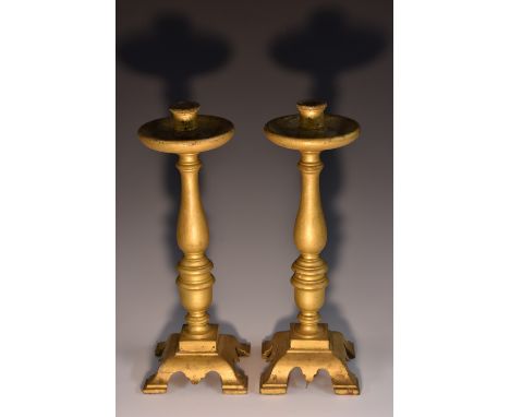 A pair of 19th century giltwood candlesticks, reel shaped sconces, broad drip pans, turned columns, square bases with bracket