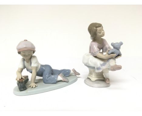 Two Lladro figures. One in the form of a girl seated holding a bear. One in the form of a boy playing with a train. Both appe