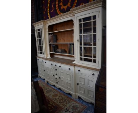 A country house breakfront library cabinet painted in buttermilk, with a central open bookcase flanked by astragal doors over