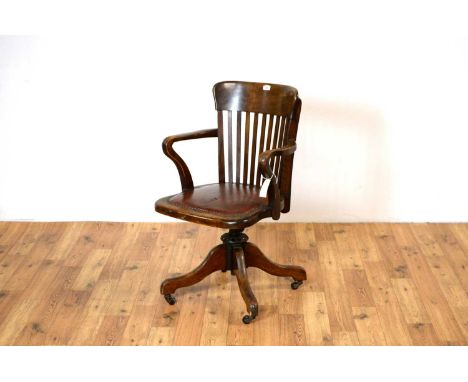 An early 20th Century oak swivel office chair, the curved crest rail with lathe back flanked by shaped elbow rests and cushio