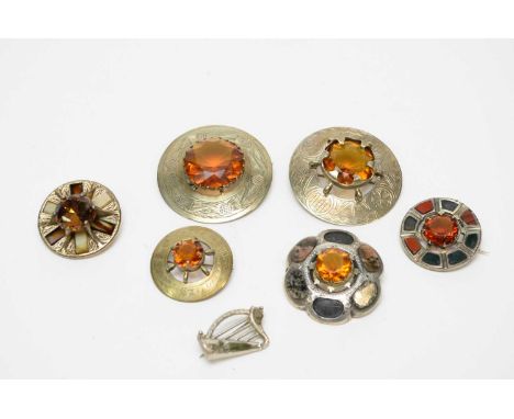 Six Scottish hard stone and paste set brooches, the largest 6cms diameter; together with a silver harp brooch, with green sto