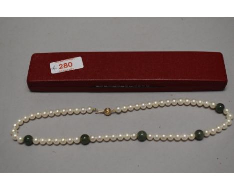 A pearl and green stone necklace, having numerous pearl beads interspersed by five green stone beads, all finishing with a ba