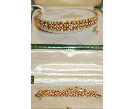 A 15ct gold, ruby and seed pearl set hinged bangle, Bannockburn, with safety chain, 13.6g, dia. 6cm, in green leather fitted 