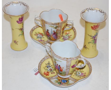 A pair of early 20th century Dresden porcelain teacups and saucers, each panel depicting a courtship scene within opposing ye