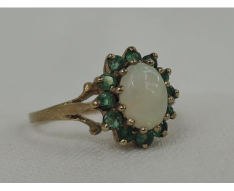 A lady's dress ring having an oval opal and emerald cluster in a raised basket mount to open shoulders on a 9ct gold loop,  s