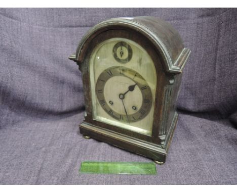 An Edwardian dark oak mantel clock having arch and faux pillar case  containing silvered dial and striking movement for T Lan