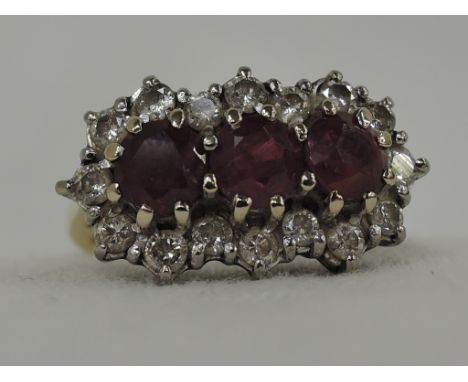 A lady's dress ring having three central rubies with a diamond surround in a raised basket mount on an 18ct gold loop,  size 