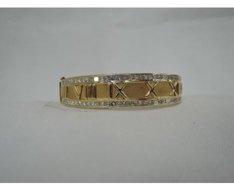 A yellow metal hinged bangle stamped 750 having moulded Roman numeral decoration and princess cut diamond set borders to one 