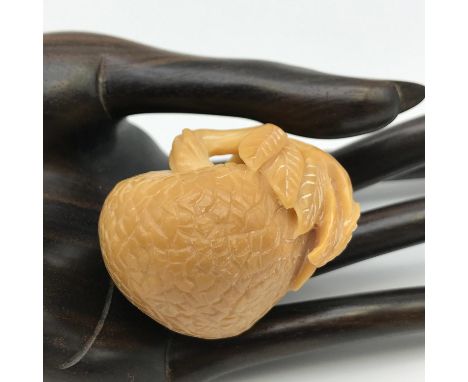 A Japanese hand carved tagua nut Netsuke. Designed into a piece of fruit with a small insect laying on a leaf. [4cm in height