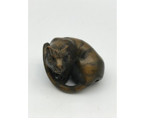 A Japanese hand carved netsuke figure of a Tiger. Detailed with black bead eyes and signed by the artist. 