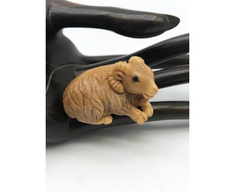 A Japanese hand carved Tagua nut netsuke figure of a goat laying down. Detailed with black bead eyes. No signature. 