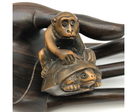A Japanese hand carved netsuke figure of a monkey sat upon a turtle. Both detailed with black bead eyes and signed by the art