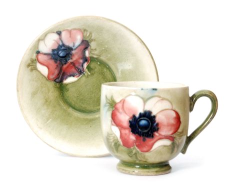 A Moorcroft coffee cup and saucer decorated in the Anemone pattern with a tubelined flower against a green wash ground, impre