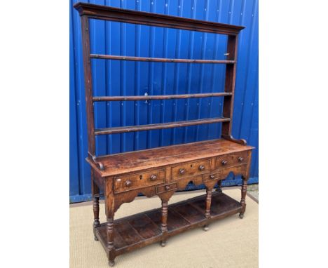 An early 19th Century oak dresser, the three tier open plate rack with moulded cornice over various cup hooks on a base of th