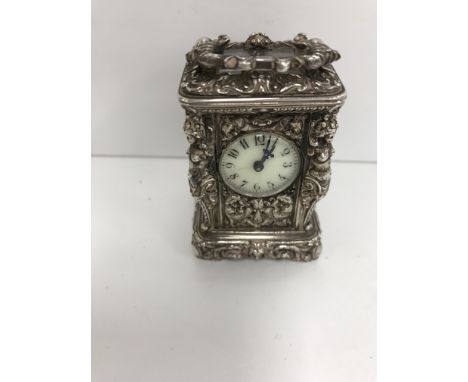 A French cast white metal cased miniature carriage clock with visible escapement and white circular dial, the chapter ring wi