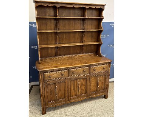An Ercol elm dresser, the three tier boarded plate rack over three drawers and three twin panelled cupboard doors on stile su