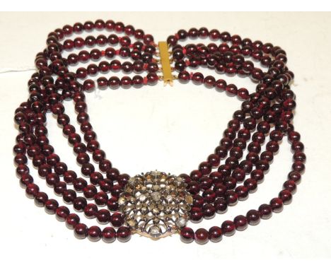 A five strand, garnet bead choker necklace, with a large yellow metal clasp set with a cluster of assorted old cut diamonds, 