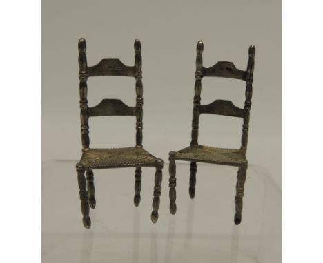 A pair of 19th Century Dutch hand made silver miniature ladder back chairs with turned supports and "rush" seats, small sword