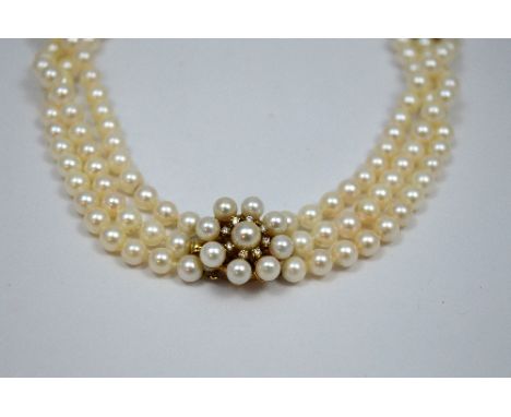 A DIAMOND AND PEARL CHOKER NECKLACE, with three strands of white pearls to the diamond and pearl flower shaped clasp, hallmar