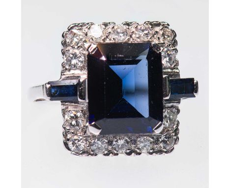 A SAPPHIRE AND DIAMOND CLUSTER RING  an octagonal-cut sapphire spaced by baguette-cut sapphires and within a border of brilli