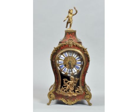 A late 19c French mantle clock in waisted red boullework case with gilt brass feet and mounts, surmounted by a putto holding 