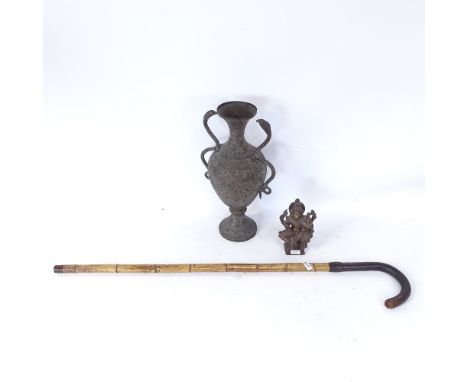 A small Buddhist bronze deity sculpture, a heavily engraved brass 2-handled urn, and a leather-handled walking stick (3) 