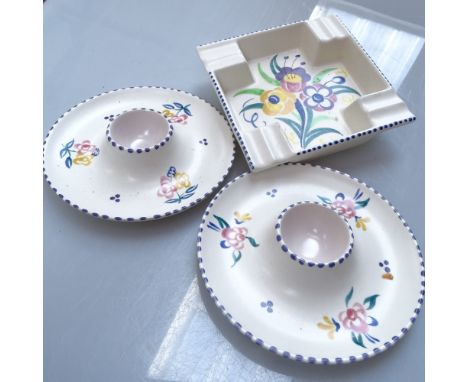 Poole Pottery plates with painted floral and bird decoration, egg cups, and an ashtray 