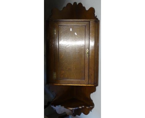 A Georgian oak hanging corner cupboard, with panelled door and shelf under, L140cm 