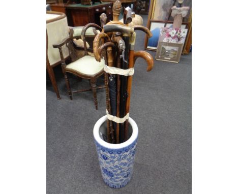 A blue and white oriental style glazed ceramic stick stand containing a quantity of vintage walking sticks and parasols 