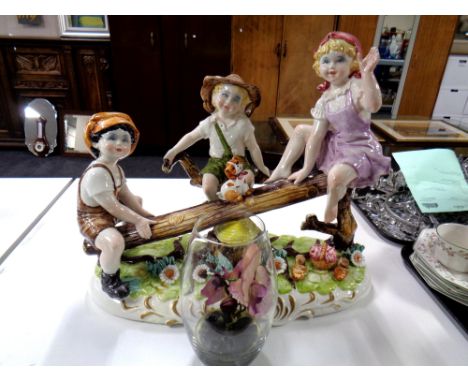 A large Capodimonte ceramic figure group of children on a wooden see-saw together with an orchid in glass vase