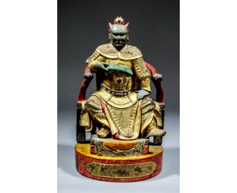 A Chinese carved polychrome and giltwood seated figure of a demon god with green painted face, his right hand holding his sas