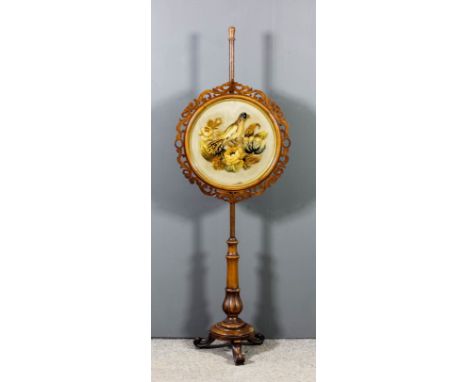 A Victorian walnut pole screen with circular panel, with moulded, fretted and carved scroll frame, and inset with woolwork pi