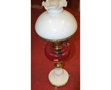 A late Victorian oil lamp having opalescent glass shade above cranberry glass reservoir on reeded glass base and brass lions 