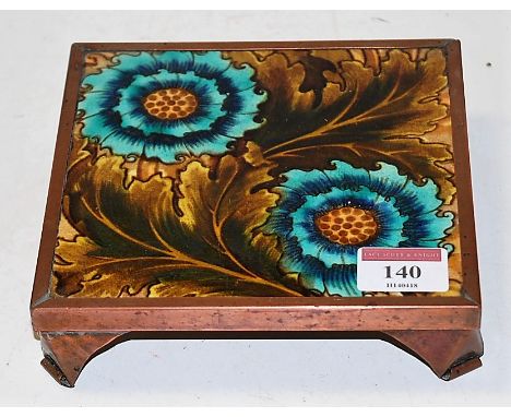 An Art Nouveau ceramic tile depicting sunflowers within laurel leaves, the whole mounted in a copper surround, 15x15cm
